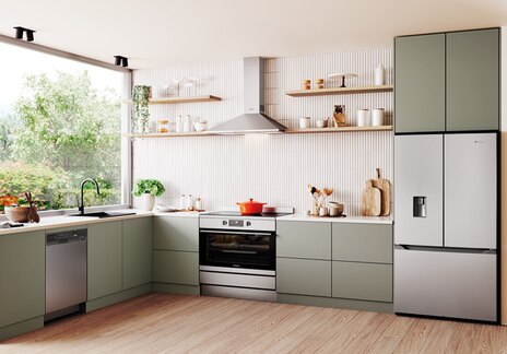 Australian kitchen with stainless steel appliances including a dishwasher, built-in oven, and French door fridge, featuring dark grey cabinets, white countertops, and garden-facing windows.